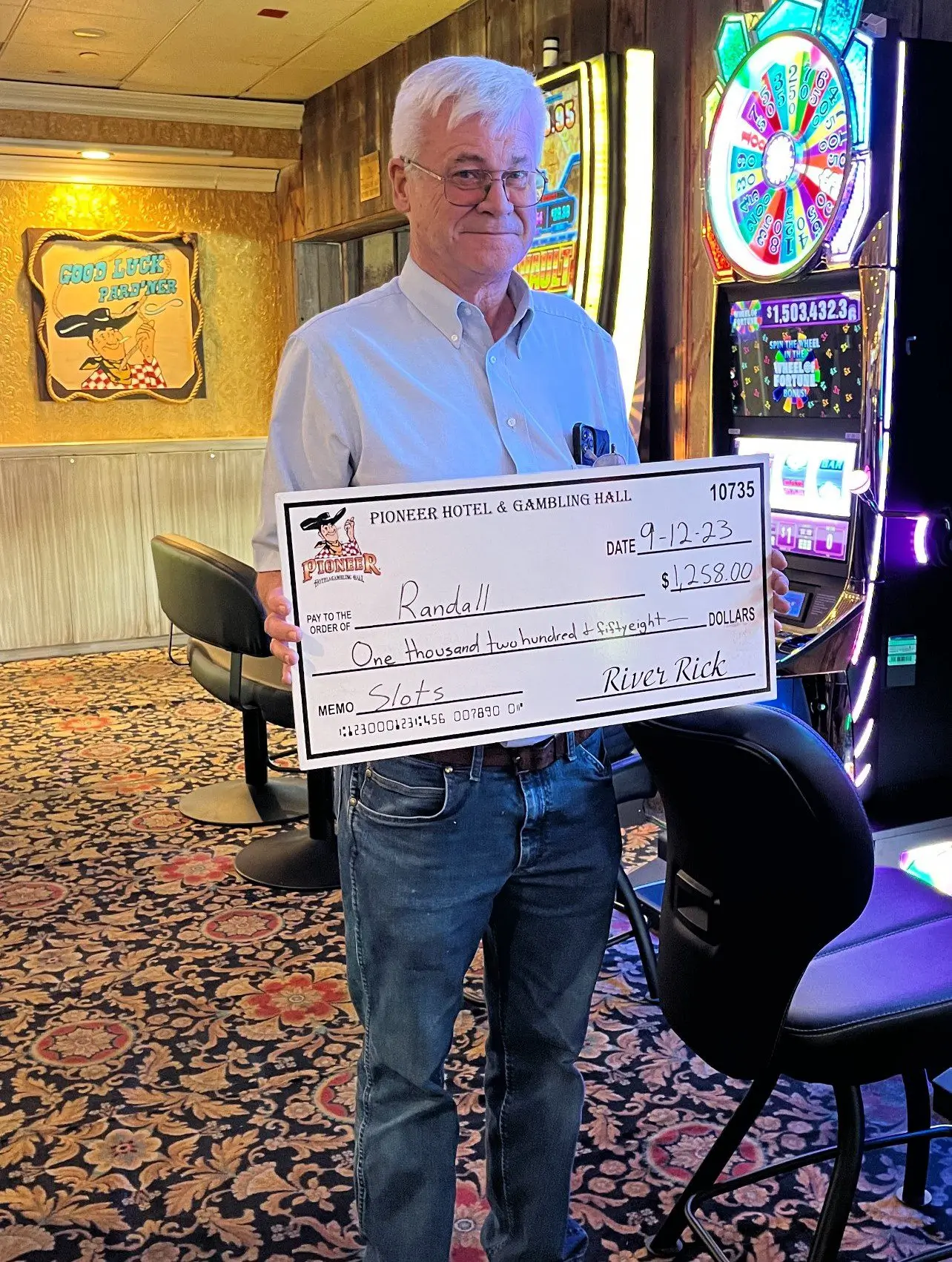 A man holding up a large check in front of a slot machine.